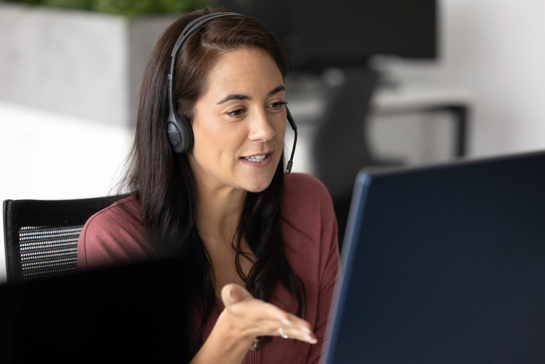 En kvinna framför datorn pratar i headset