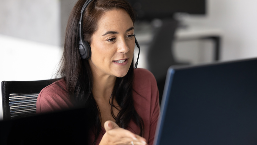 En kvinna framför datorn pratar i headset