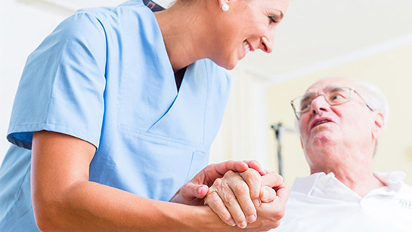 En kvinna som jobbar inom vården håller en äldre persons hand