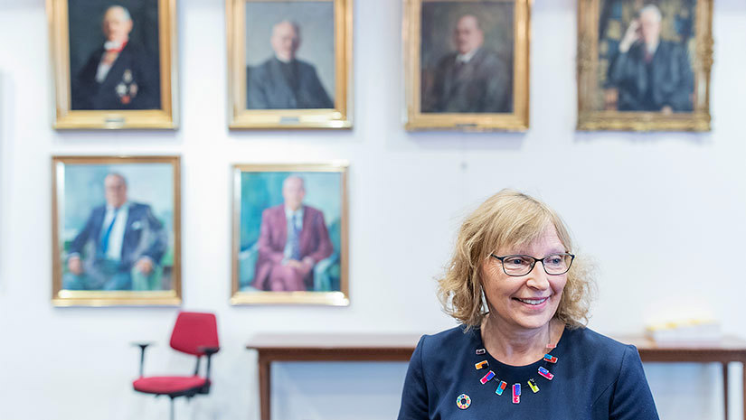 Politikern Carina Nilsson framför en vägg med tavlor med olika män. 