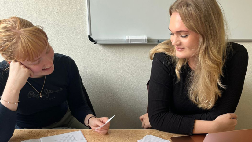 Elin Holmström och Leonella Ahlén sitter vid ett bord med en dator och papper framför sig