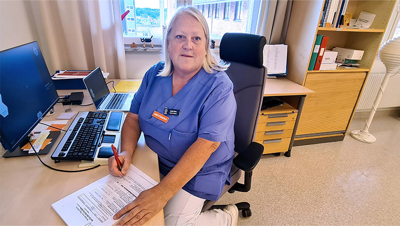 Kerstin Kåwe sitter vid ett skrivbord med papper och penna för händerna. 