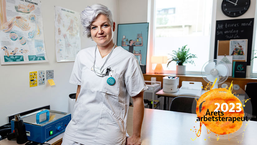 Catrin Knutsson står lutad mot ett bord på sin arbetsplats och ler in i kameran. 
