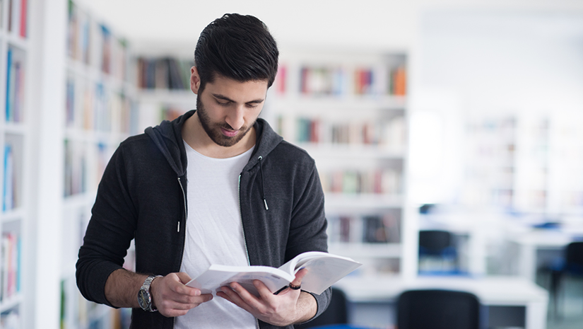Person som står i ett bibliotek, läser en bok