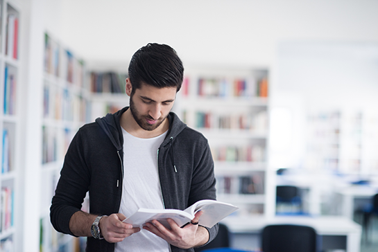 Person som står i ett bibliotek, läser en bok