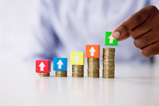 En uppåtgående trappa av mynt och en person som lägger klossar med pilar på ovanpå